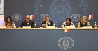 Five officials at a panel desk during a formal press conference, with Italian flags and a government seal backdrop.