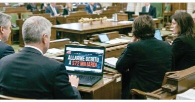 Politicians in a parliamentary chamber, a laptop on a desk shows a headline about debt alarm in Italian.”] ,