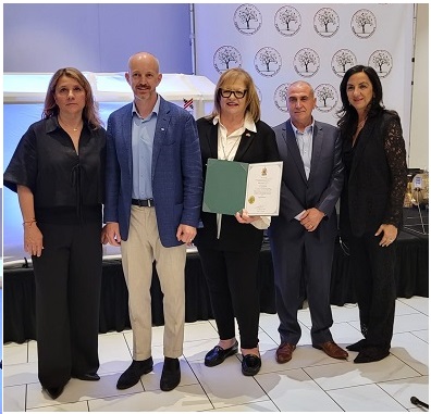 Five adults pose for a photo at an award ceremony; center woman holds a green certificate.