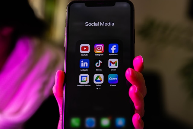 Hand holding a smartphone displaying a grid of social media app icons under the label 'Social Media'.