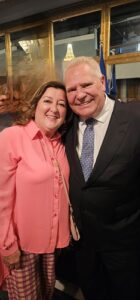 Smiling couple posing for a photo at a formal event; woman in a pink blouse, man in a dark suit.