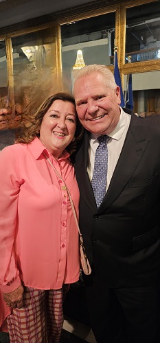 Smiling couple posing for a photo at a formal event; woman in a pink blouse, man in a dark suit.