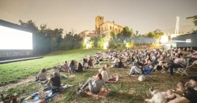 Crowd seated on blankets watching an outdoor movie on a large screen, with a lit historic building in the background.
