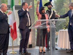 Group of officials raising glasses in a toast at a formal event, Italian flag in the background