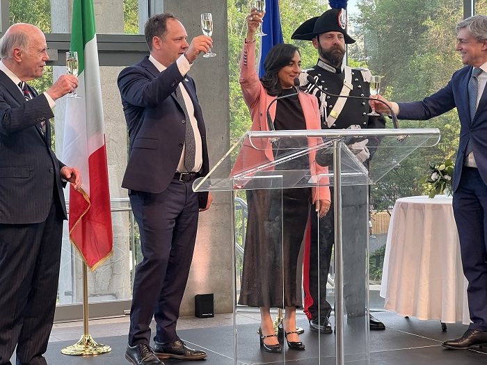 Group of officials raising glasses in a toast at a formal event, Italian flag in the background