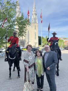 Four people pose for a photo in front of a cathedral, with two guards on horseback in red uniform standing nearby.