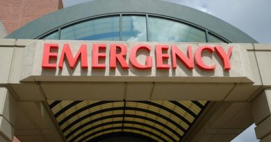 Hospital emergency department entrance with a large red 'EMERGENCY' sign over a glass curved canopy, at the building's facade.
