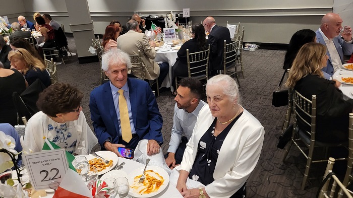 Group of five adults seated at a round banquet table, enjoying plates of food at a formal event.