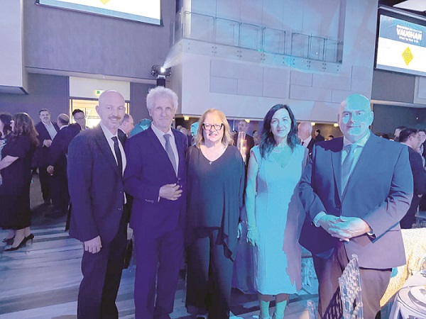 Five professionally dressed people pose together for a photo at a formal cocktail event in a modern venue.