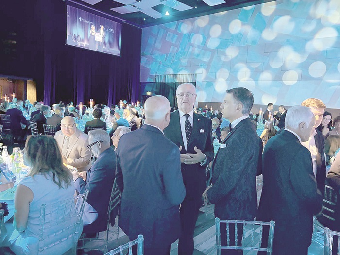 Groups of professionals in suits chatting at a formal banquet in a blue-lit conference hall with round tables.