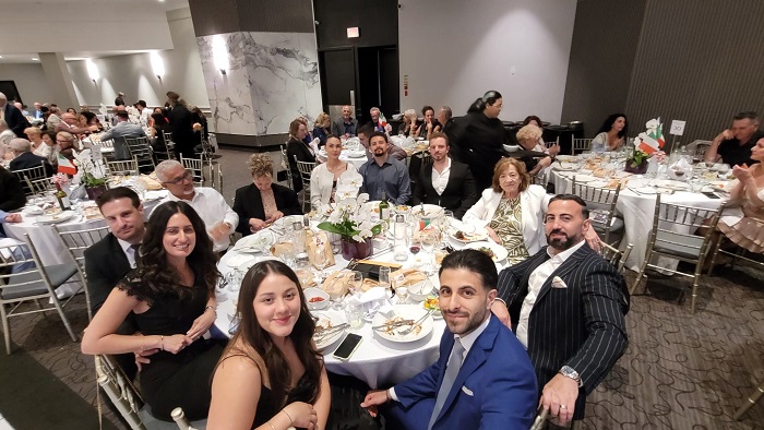 Eight people in formal wear sit around a round banquet table with a small floral centerpiece at a catered event.