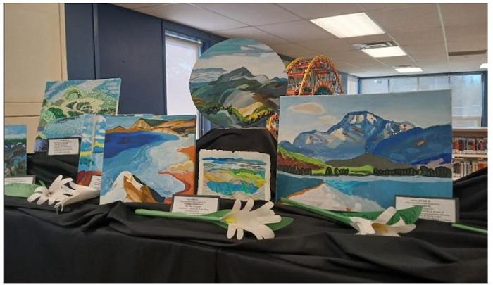 Display of landscape paintings arranged on a black-cloth table in a room, including a round mountain scene and a few white decorative flowers in the foreground.