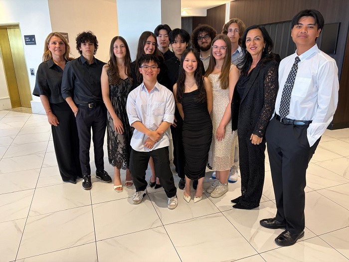 Group of students and adults in formal attire posing together in a bright indoor hallway or lobby.