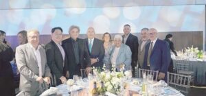 Group of professionally dressed people posing together at a banquet table with white flower centerpiece and place settings.