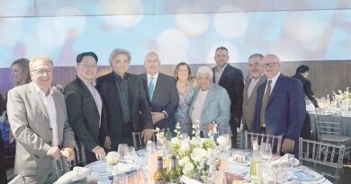 Group of professionally dressed people posing together at a banquet table with white flower centerpiece and place settings.
