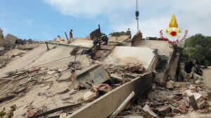 Firefighters conduct a rescue amid collapsed building debris on a rubble slope, with a crane overhead.