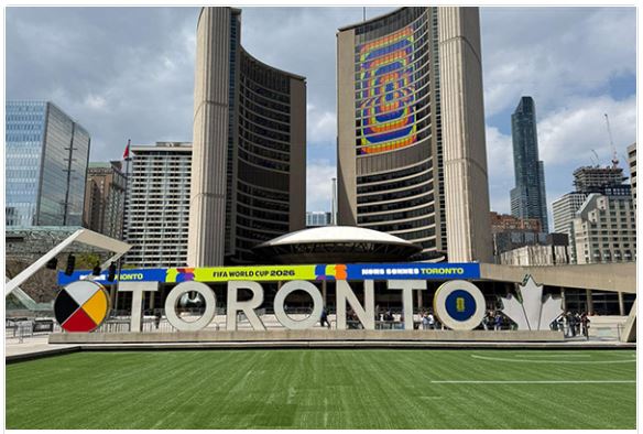 Toronto sign with large TO RONTO letters in front of tall buildings and a football field, celebrating FIFA World Cup 2026 in Toronto