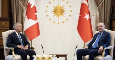 Two world leaders sit in ornate chairs for a formal diplomatic meeting, with Canadian and Turkish flags behind them and a sun emblem in the center.