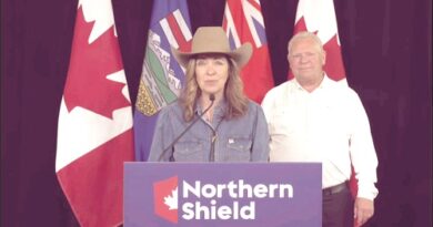 Woman wearing a cowboy hat and denim shirt speaks at a podium labeled 'Northern Shield' with flags behind her.