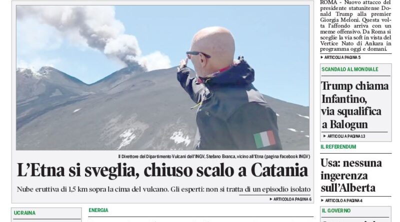 Man in a dark jacket standing on snow on Mount Etna with smoke rising from the crater behind him.