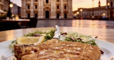 Close-up of a crispy breaded schnitzel on a plate with a lemon wedge and greens, set outdoors against a sunset square and a grand cathedral in the distance.