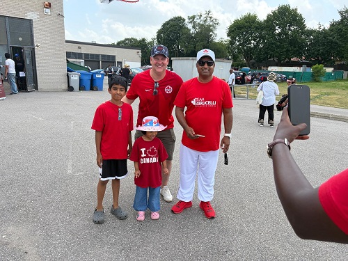 Group of four people in red shirts posing outdoors while a person in the foreground uses a smartphone to take their photo.
